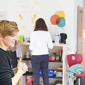 Annika Kreikenbohm im Vordergrund lächelt. Im Hintergrund sind zwei Personen zu sehen, die an der Wand stehen. 