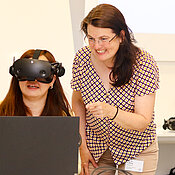Dr. Oyudari Vova testet ein VR-Programm. Sie trägt eine VR-Brille. Dr. Sarah König unterstützt sie dabei.