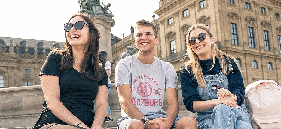 Studierende der JMU vor der Würzburger Residenz. In dem früher fürstbischöflichen Schloss und UNESCO-Welterbe sind unter anderem Philosophie-Lehrstühle und die Altertumswissenschaften der Universität zu Hause.