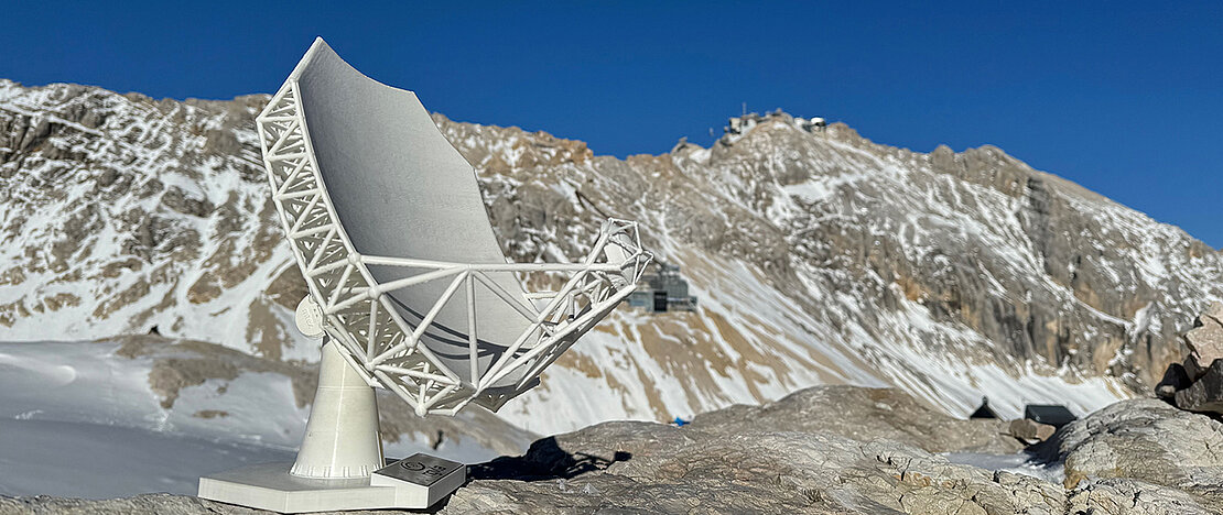 Modell des Wetterstein Millimeter Teleskops an einem der möglichen Standorte am Zugspitzplatt. Die Umweltforschungsstation ist im Hintergrund sichtbar, rund dreihundert Höhenmeter unterhalb des Gipfels der Zugspitze. 